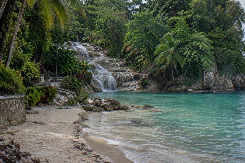 Calm sandy beach at the base of a waterfall where it meets the Caribbean sea