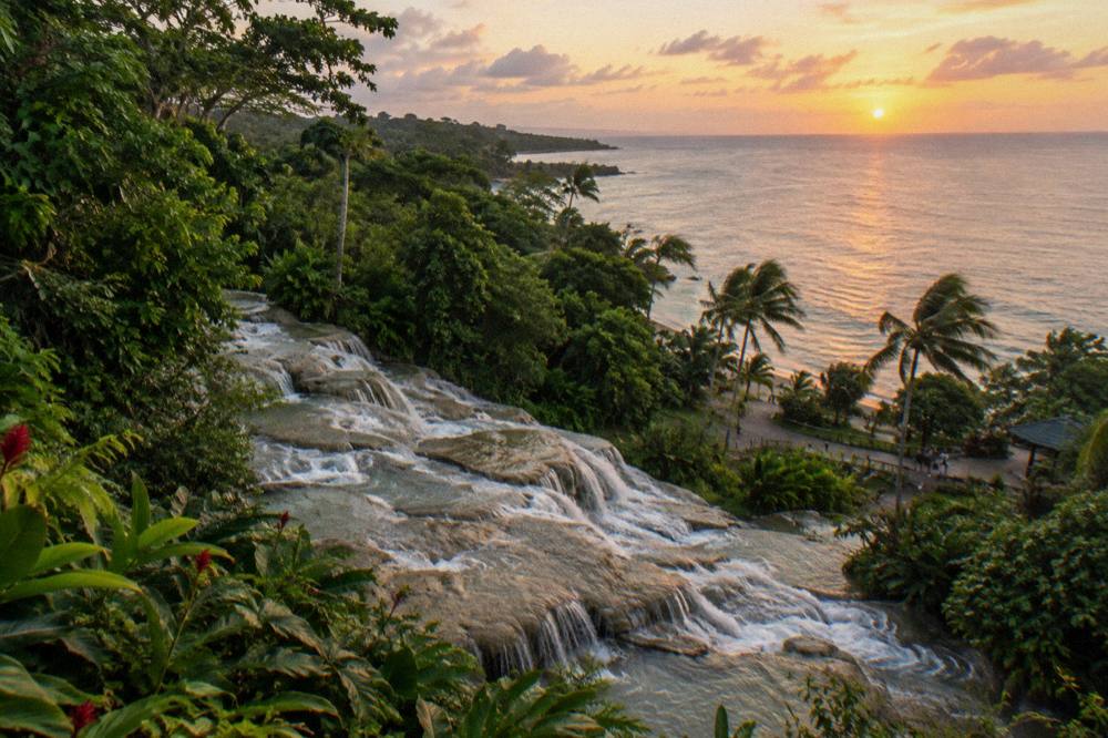 Waterfall terraces descending through tropical greenery toward the Caribbean coastline