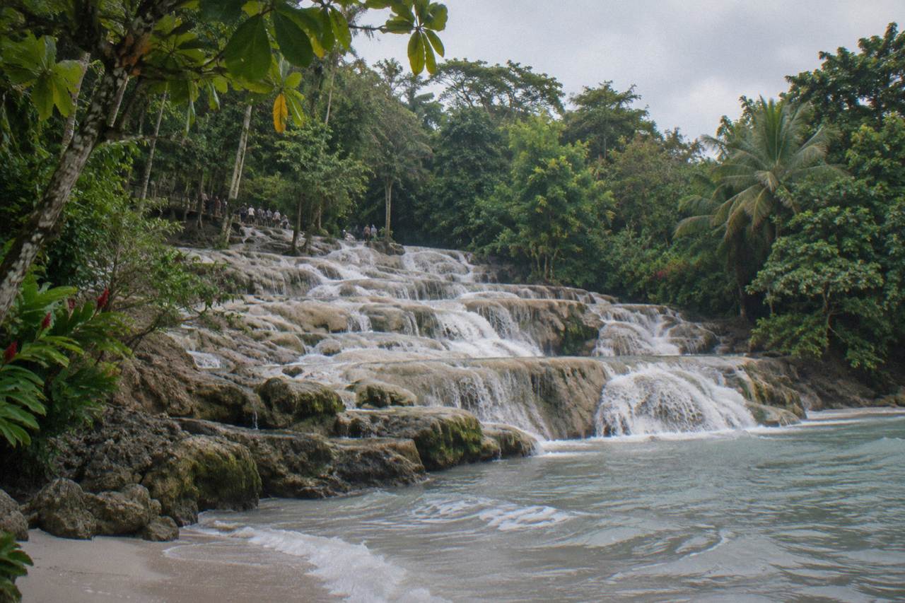 Terraced waterfall cascading over pale rock steps toward a beach and the sea