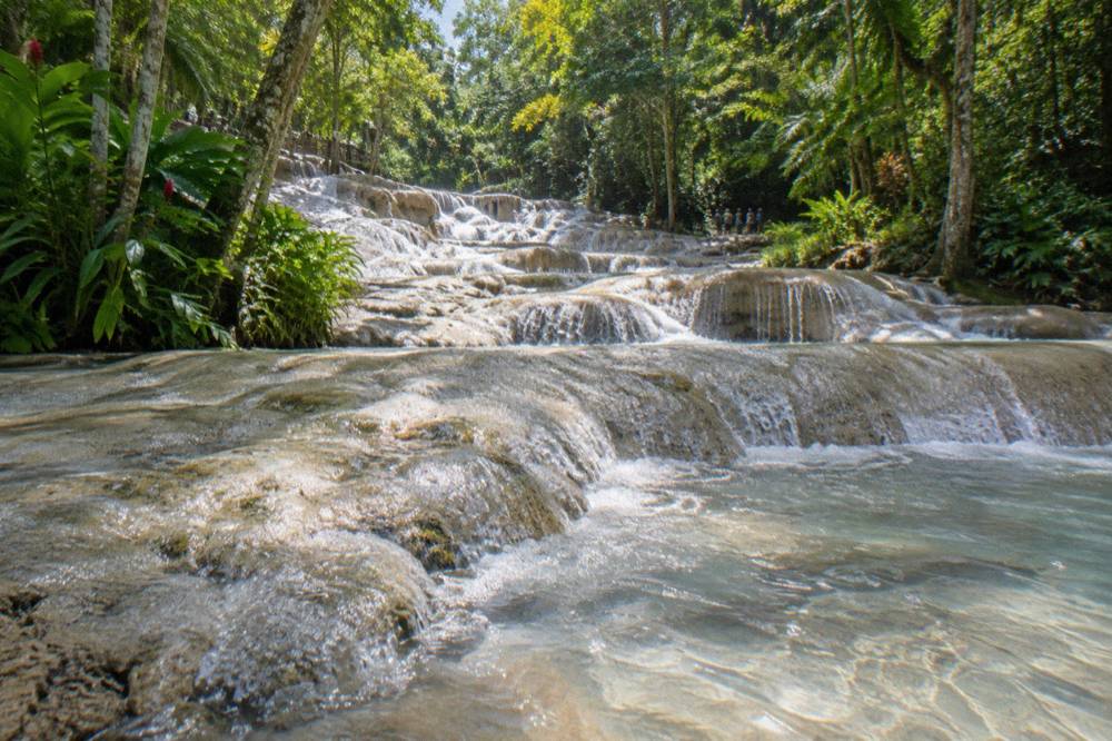 Shallow water running across pale limestone terraces at the base of a waterfall