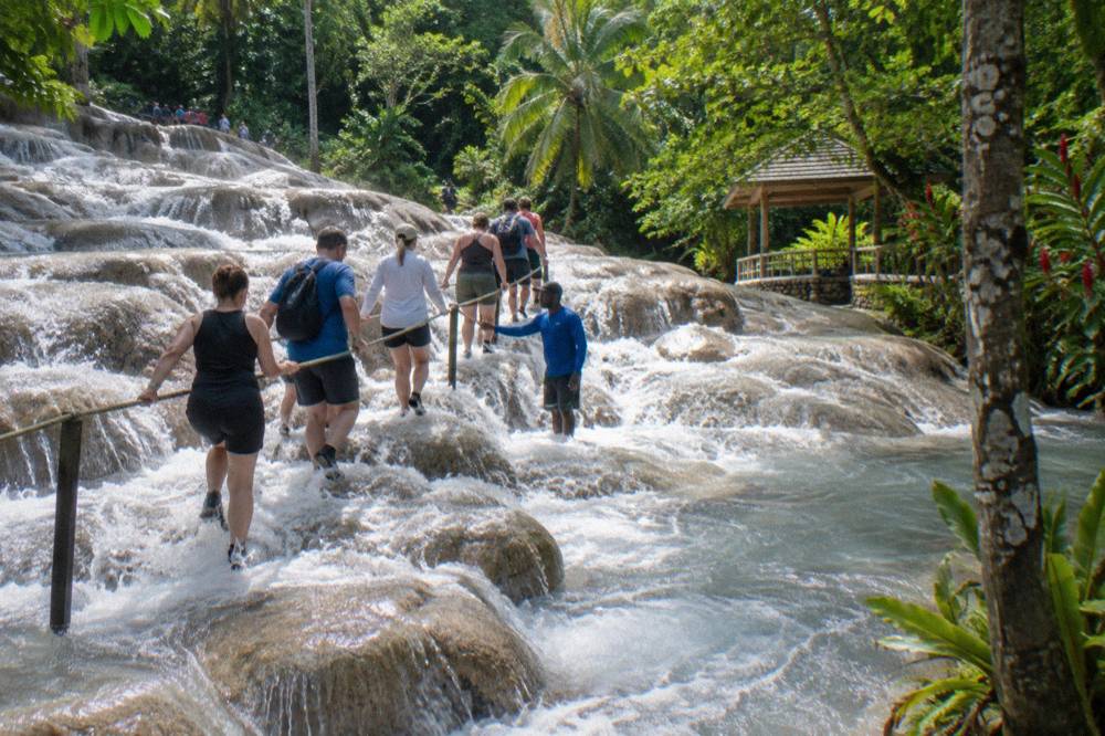 Visitors in water shoes forming a chain as they climb a stepped limestone waterfall