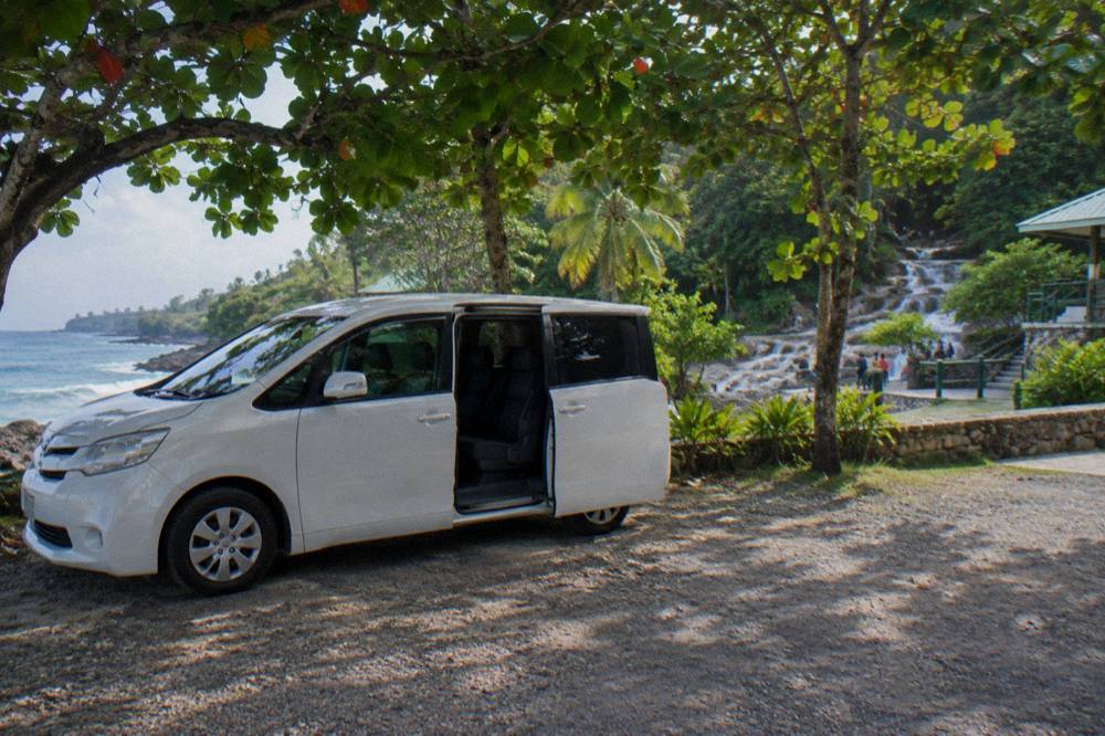 Private minivan waiting at a shaded pull-off beside a coastal highway