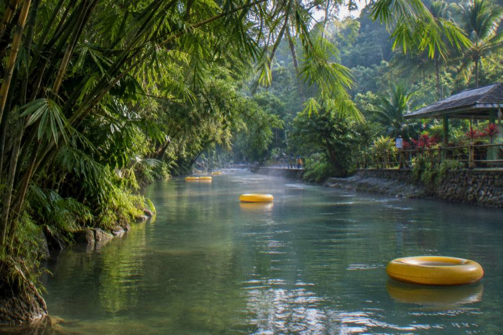 Inflatable tubes floating down a calm jungle river between overhanging trees