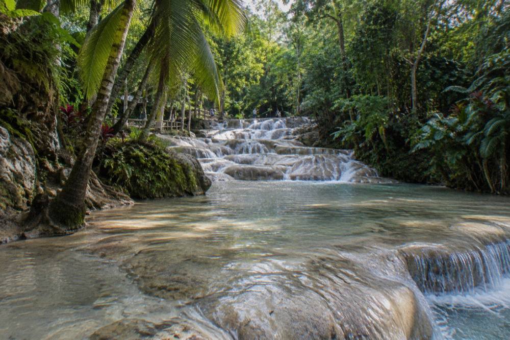Shallow natural pool on a terraced rock waterfall with water flowing over smooth stone steps