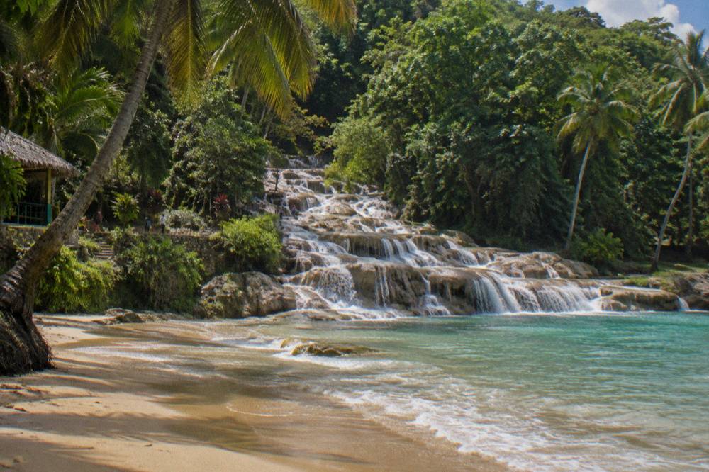 Family beach beside a tropical waterfall with calm shallow water and palm trees