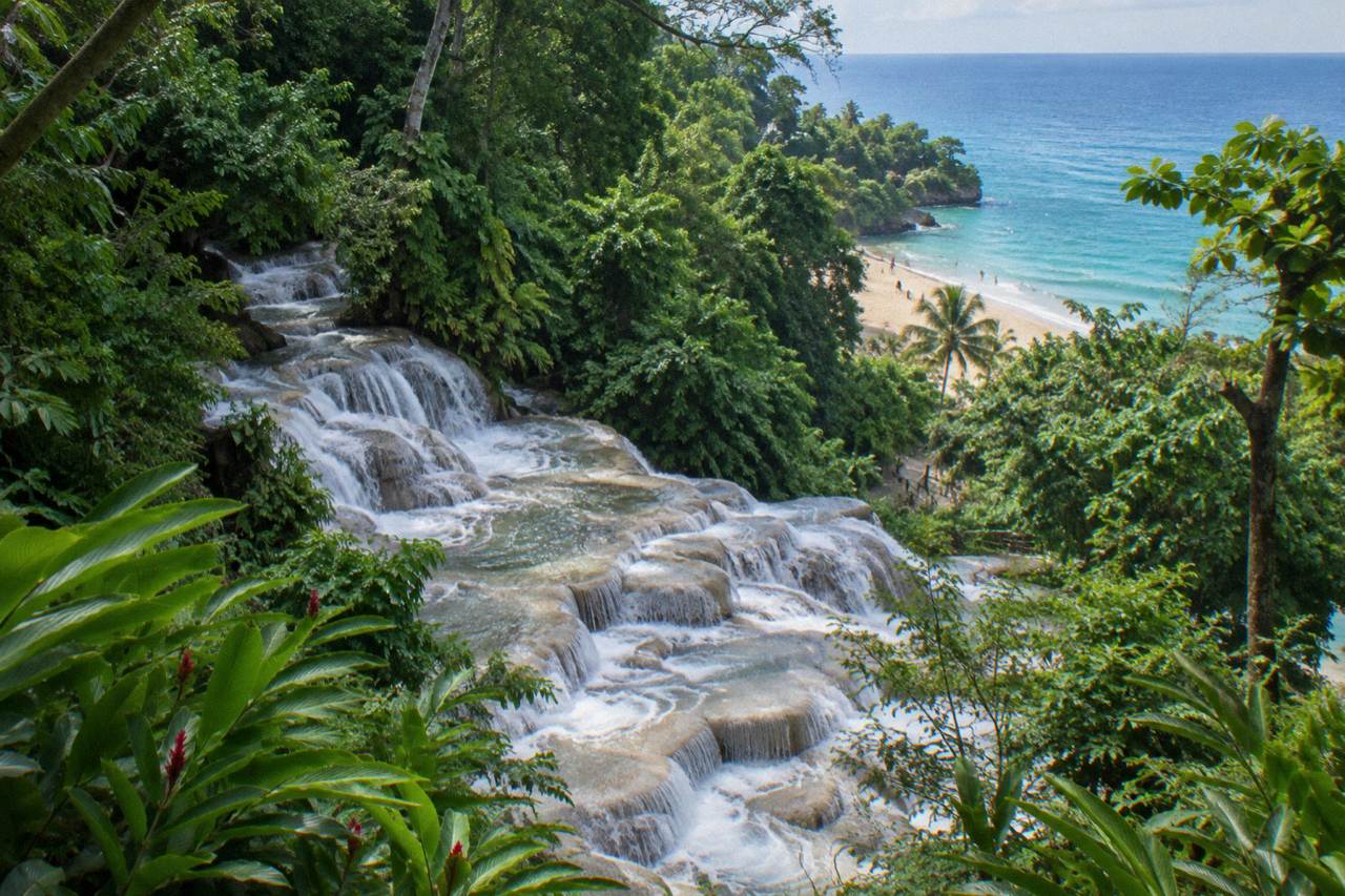 Terraced waterfall cascading through a green tropical park toward a small beach