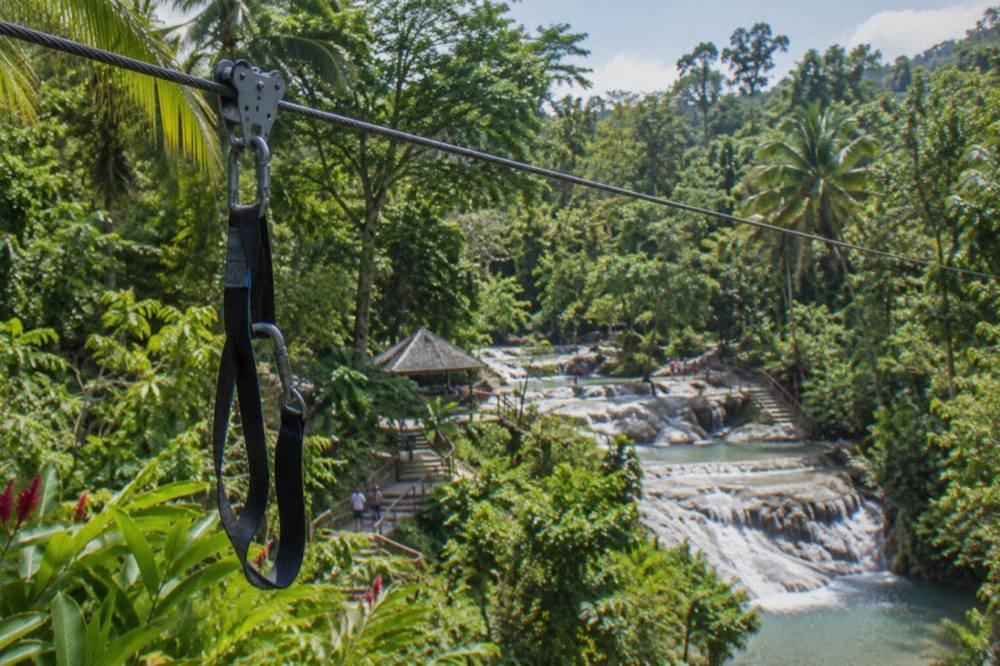 Zipline cable stretched over green tropical foliage near a waterfall