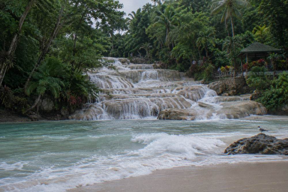Small sandy beach at the base of a waterfall where fresh water meets the Caribbean sea