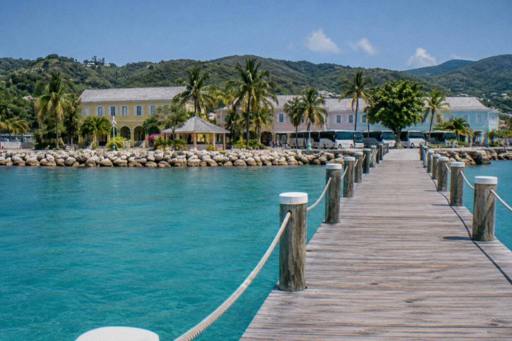 Wooden cruise ship pier extending into turquoise harbor water with tour buses parked on shore