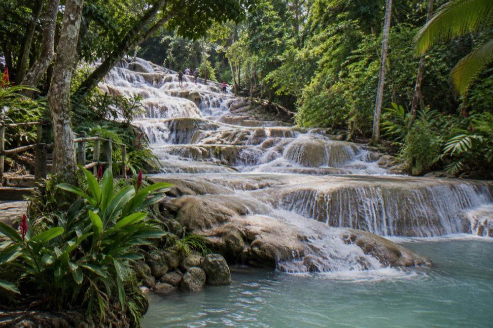 Tourists in swimwear climbing a terraced waterfall in a line holding hands