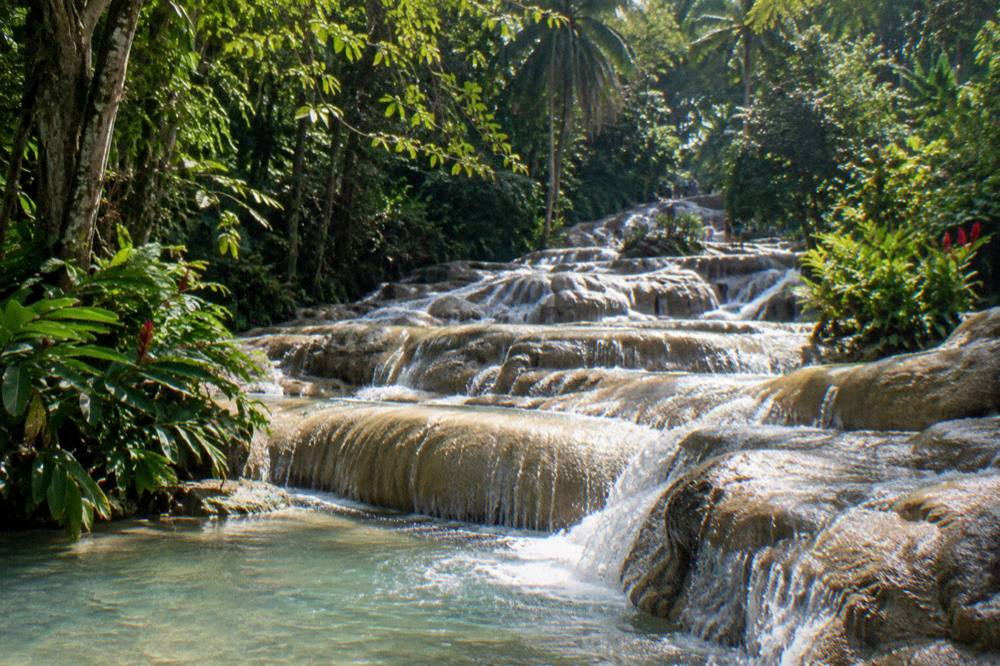 Guided group forming a human chain while climbing a waterfall terrace in Jamaica