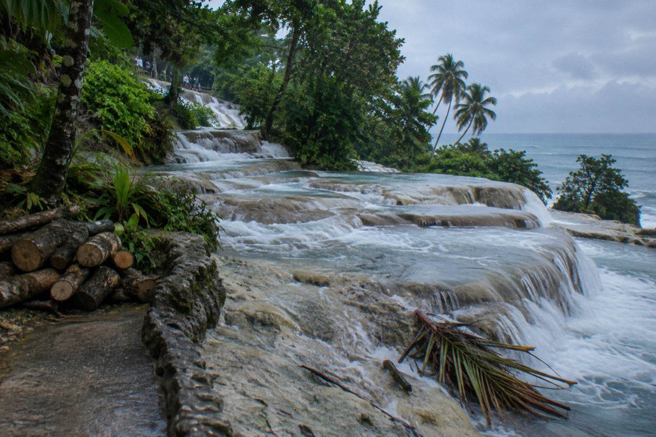 Waterfalls cascading down limestone terraces toward a beach and the sea at Dunn's River Falls
