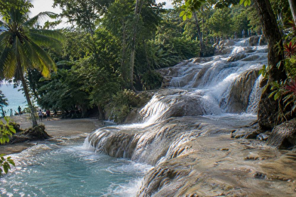 Waterfall terraces stepping down through tropical foliage toward a sandy beach