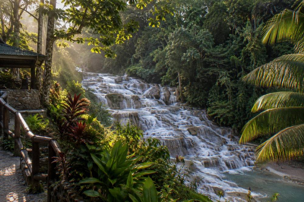 Terraced waterfall cascading in steps toward a sandy beach and calm Caribbean water