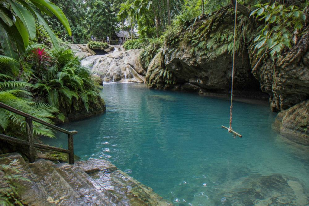 Turquoise natural pool at a jungle waterfall surrounded by ferns and rocks