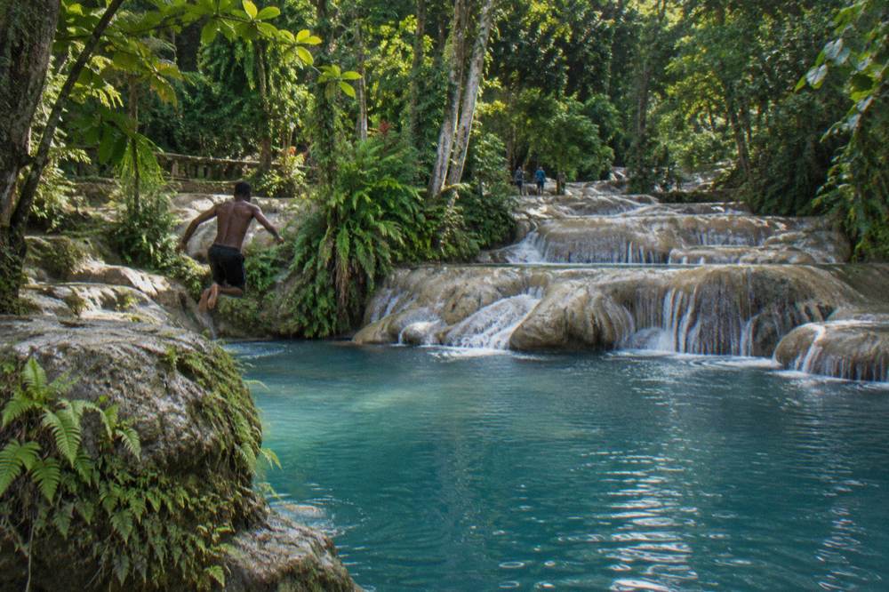 Swimmer jumping into a deep blue jungle pool below a small waterfall