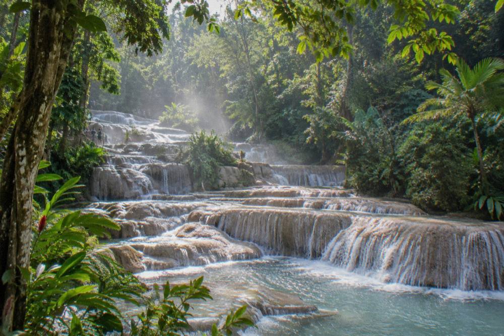 Swimmers in rash guards and water shoes forming a chain on wet limestone steps of a waterfall