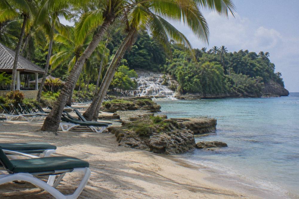 Beach chairs and palm shade at a Caribbean beach club beside calm water