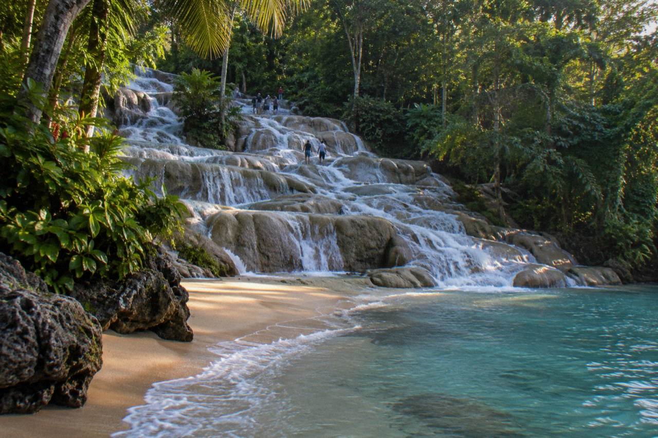 Terraced limestone waterfall steps cascading into a small sandy beach beside turquoise water