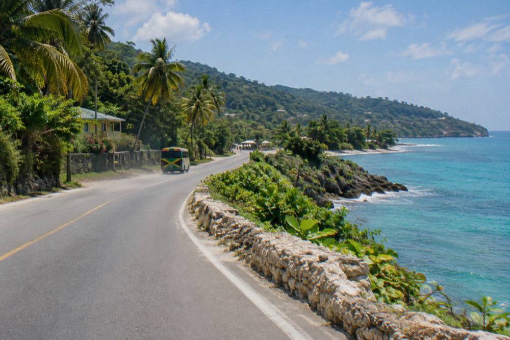 Coastal highway curving along a green shoreline with the sea on one side and palm-covered hills