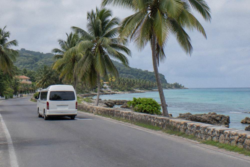 Tour van travelling a coastal road between palm trees and turquoise water