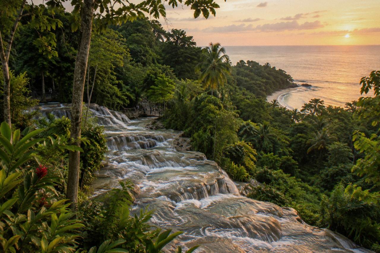 Terraced waterfall cascading through a green tropical gorge toward a small sandy beach
